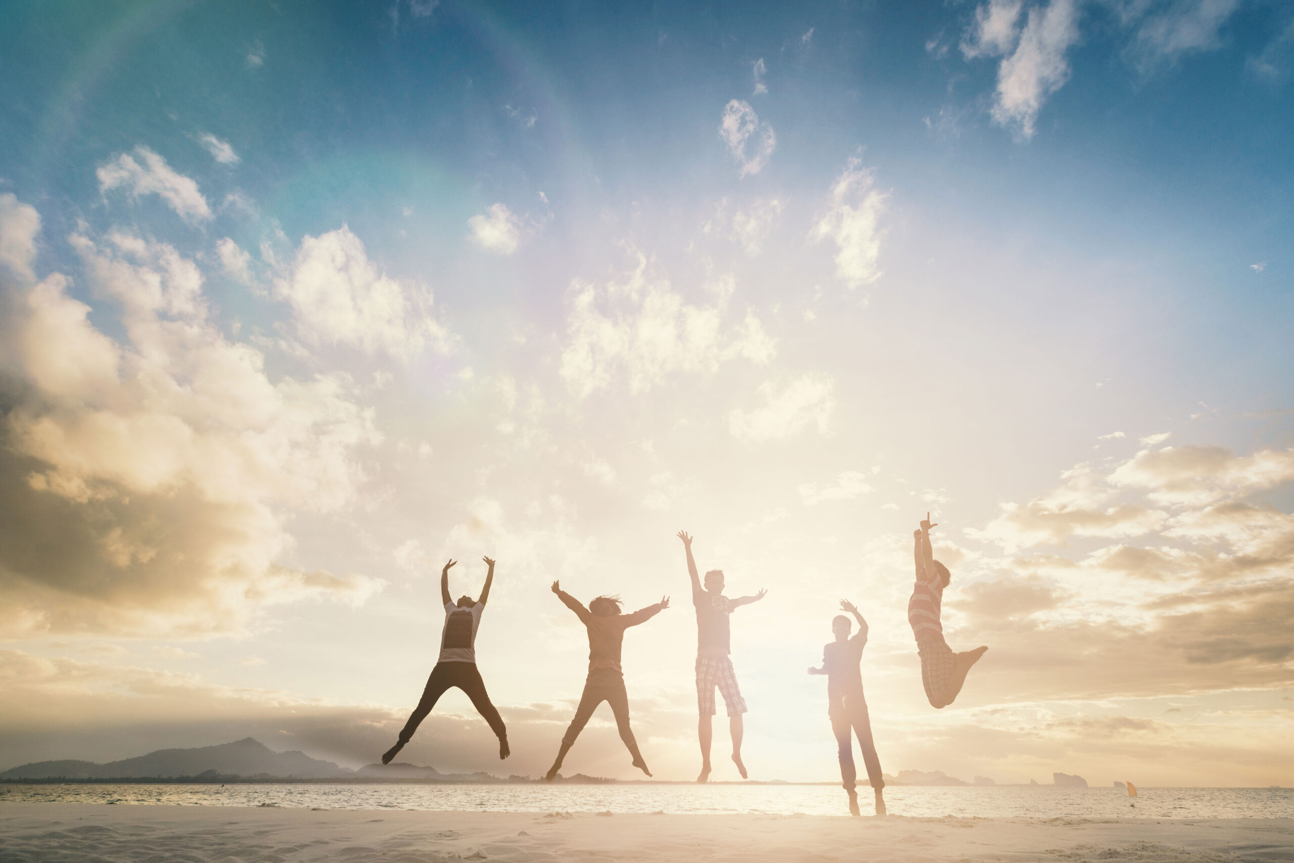 5 silhouettes jumping in the air with the ocean in the background