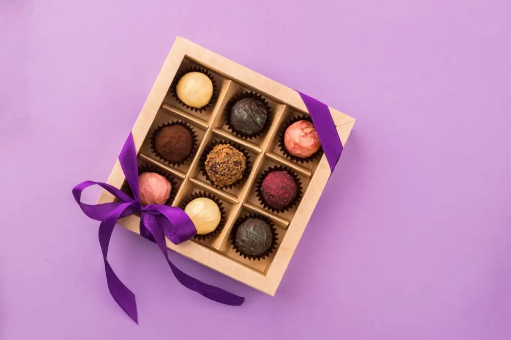 RBox of 9 assorted chocolates in a gift box wrapped in dark purple ribbon against a light purple background